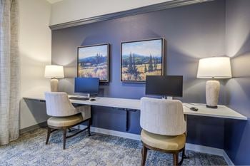 Two desks with two chairs and two computer monitors in a room with a blue wall